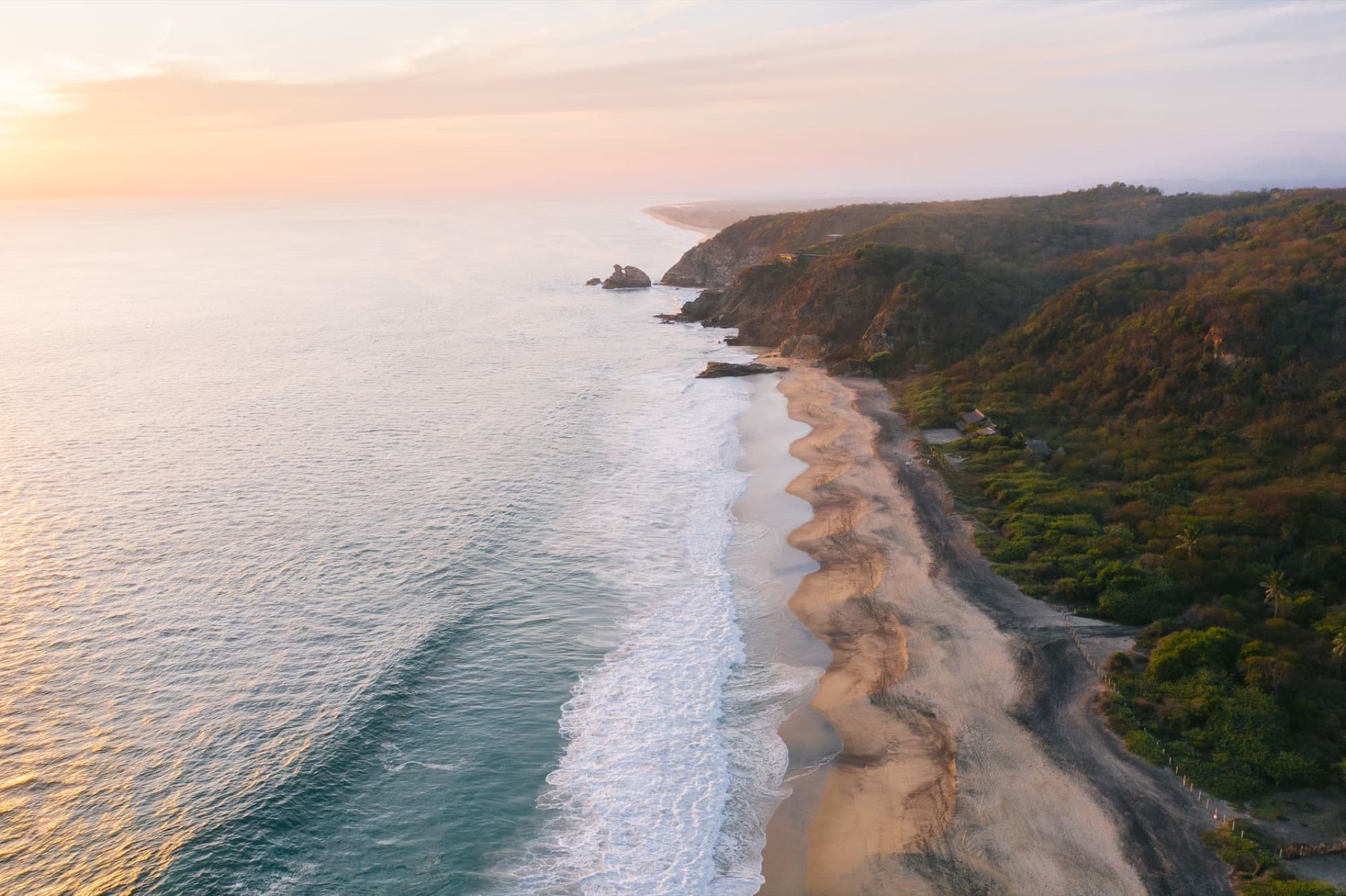A breathtaking aerial view of the Oaxaca coastline, showcasing the ocean and cliffs at sunset.