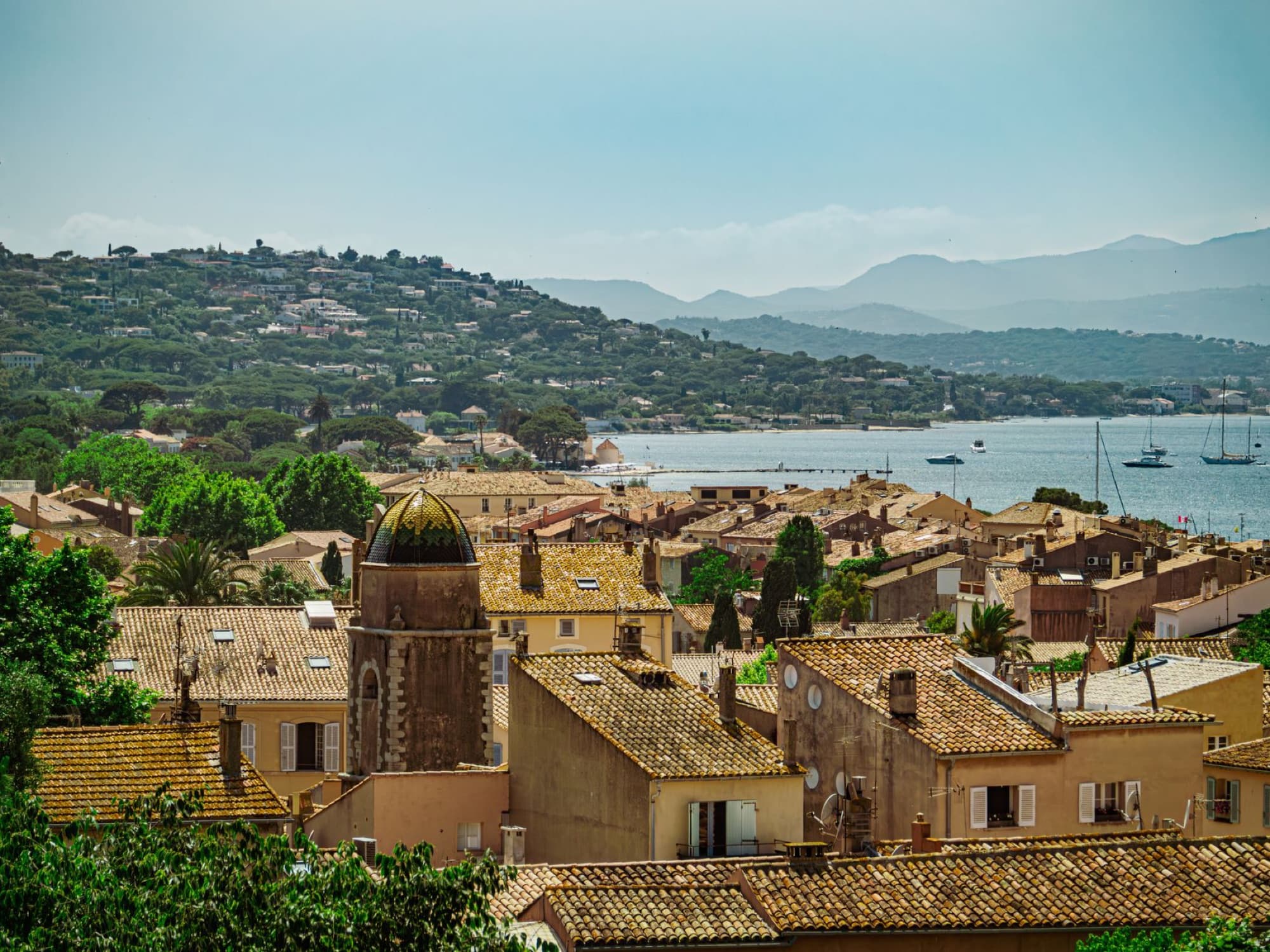 Scenic view of a coastal town in Southern France with rooftops, hills, and the sea.