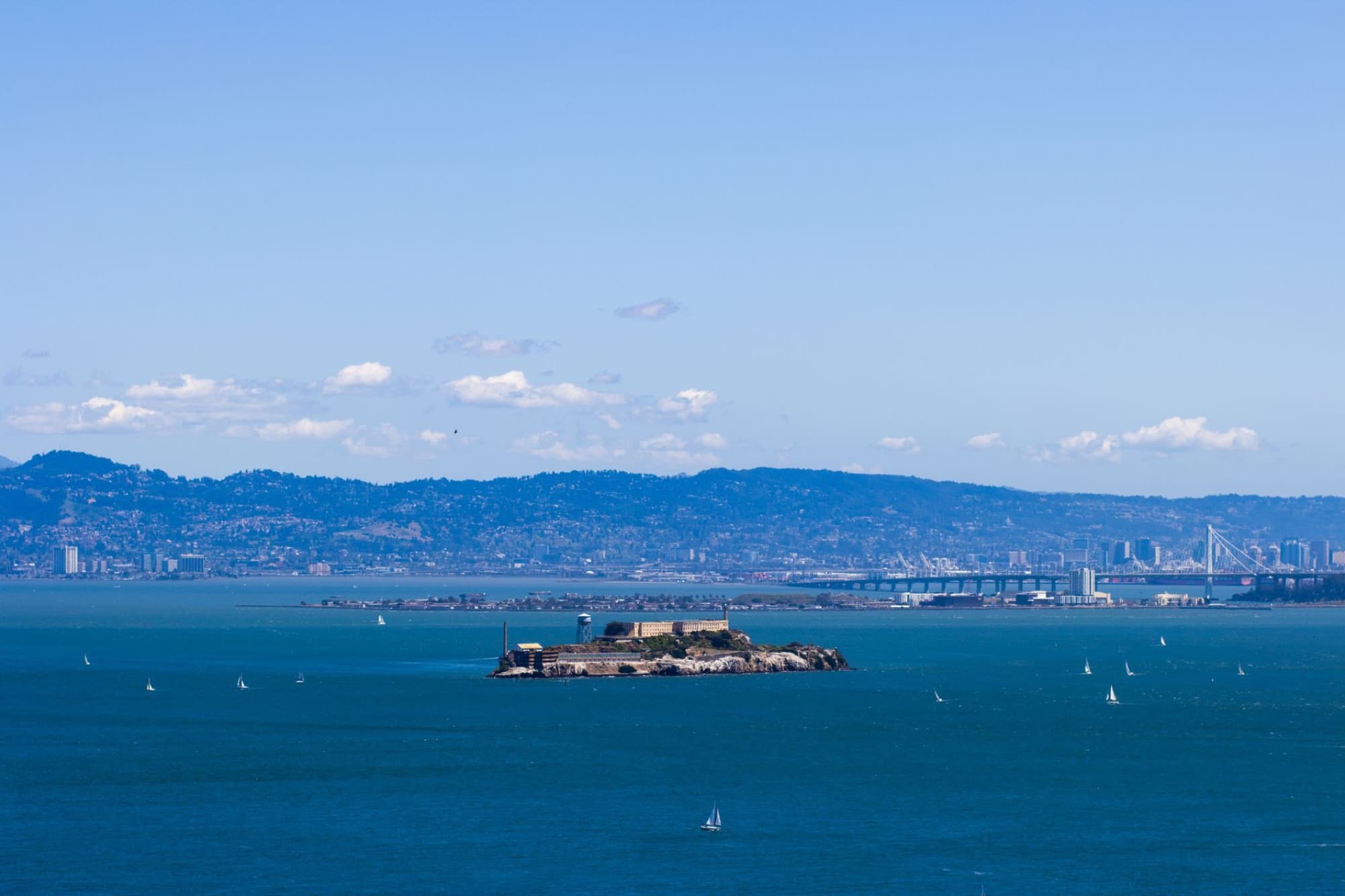 Aerial view of Alcatraz Island in San Francisco Bay with city skyline and sailing boats.