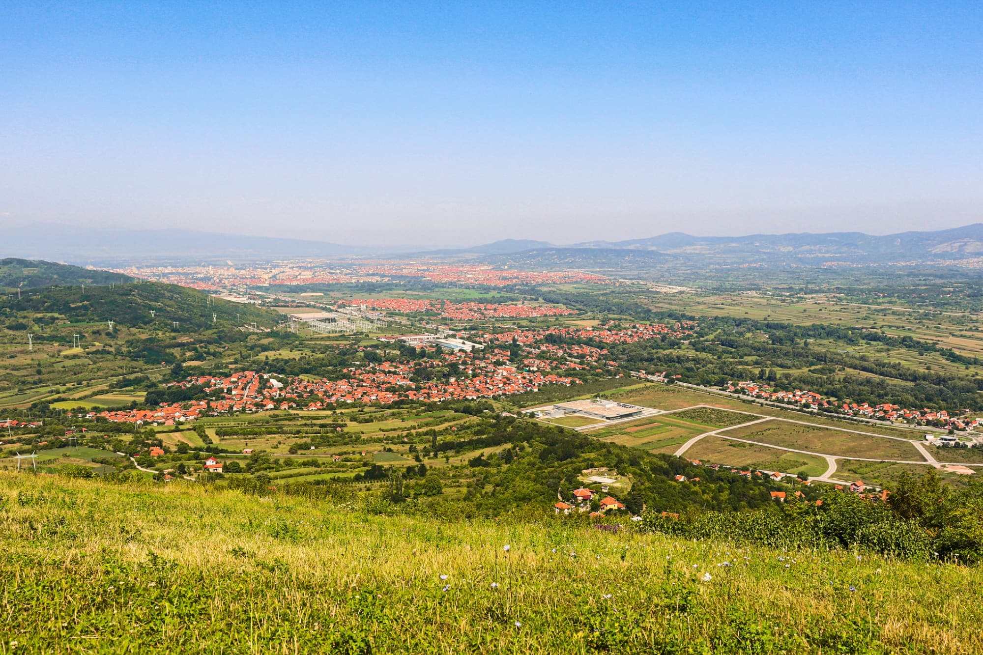 Explore a breathtaking aerial view of the verdant Niš countryside in Serbia, captured under a clear blue sky.