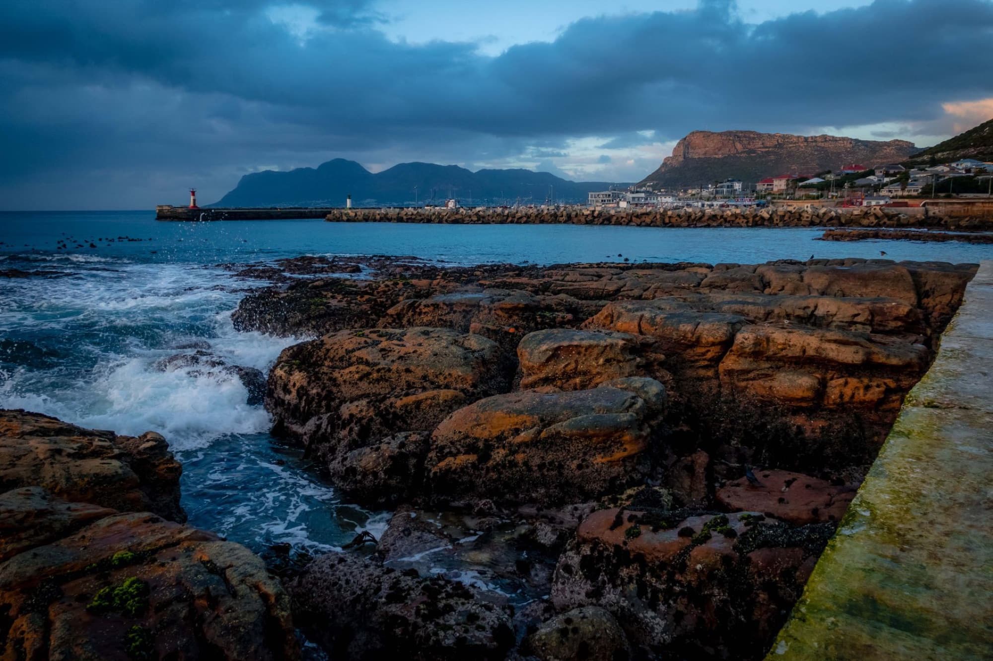 Dramatic coastal landscape with rocky shores and lighthouse at sunset in Cape Town, South Africa.