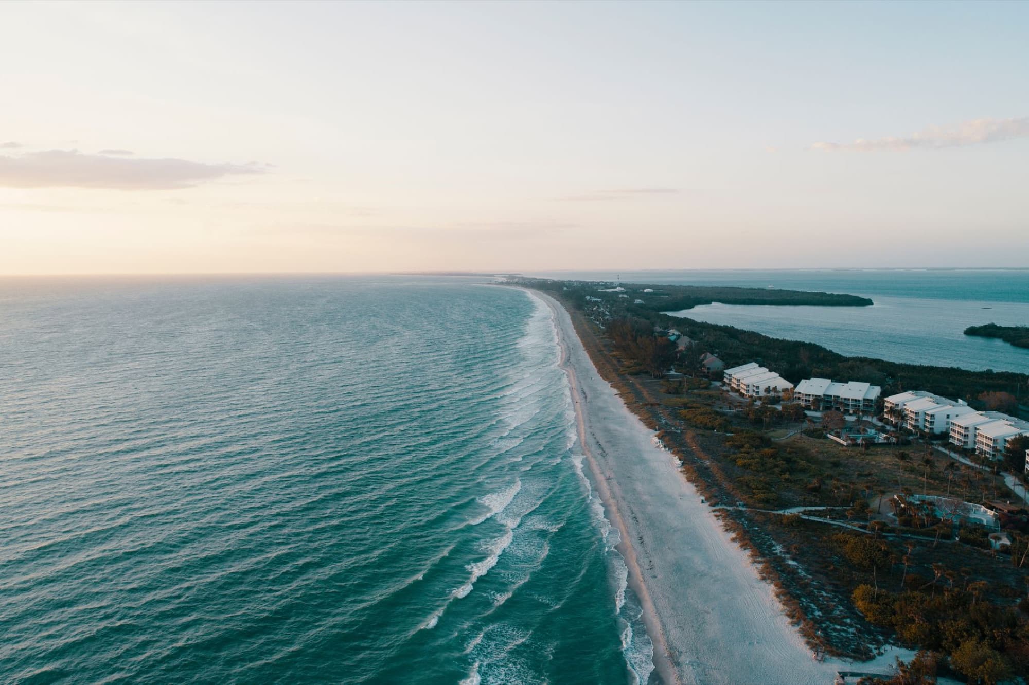 Stunning aerial view of a serene beach coastline at sunset with ocean waves and distant horizon.