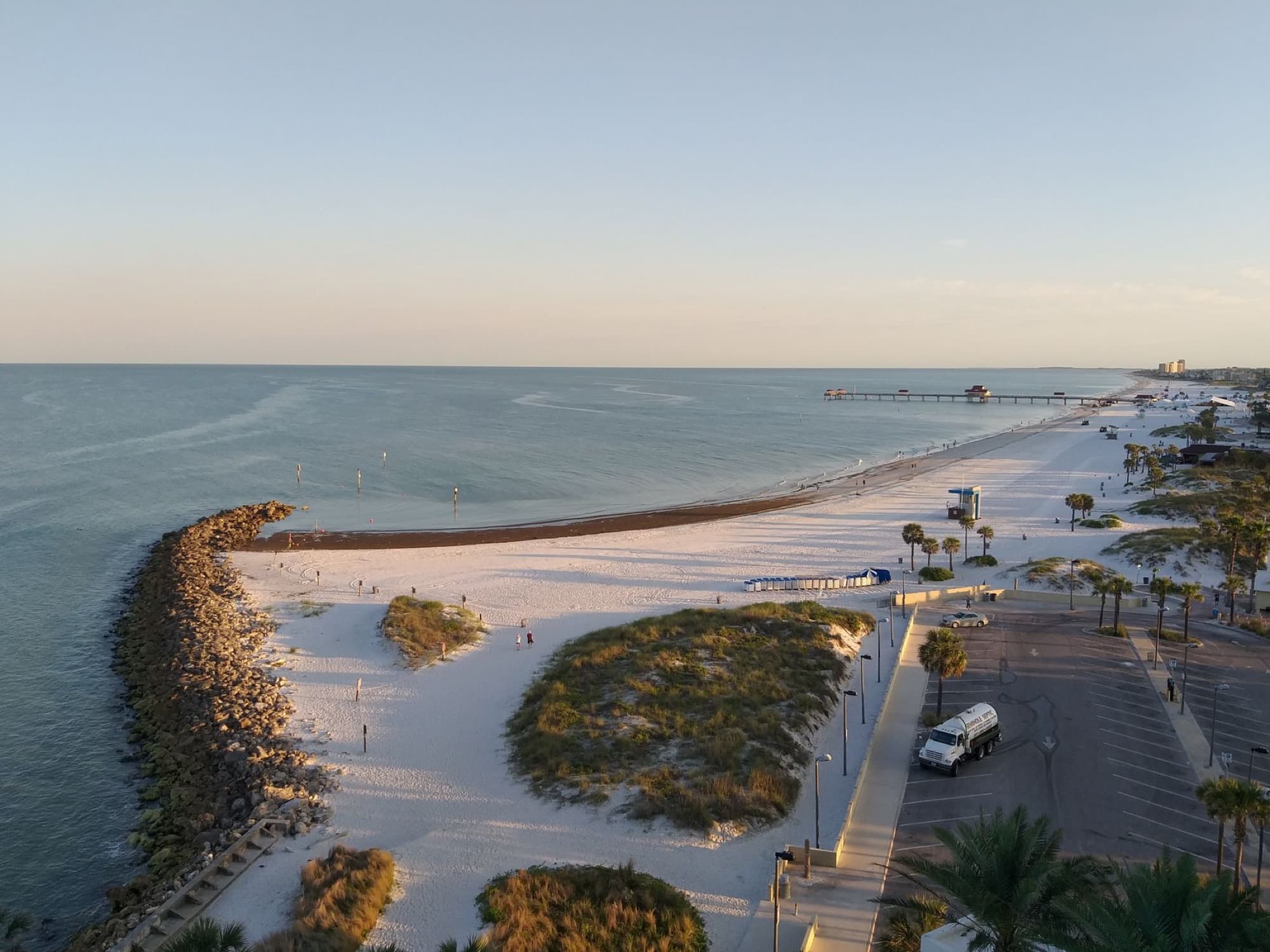 Stunning aerial view of a sandy beach with a pier at sunset, showcasing the tranquil seaside atmosphere.