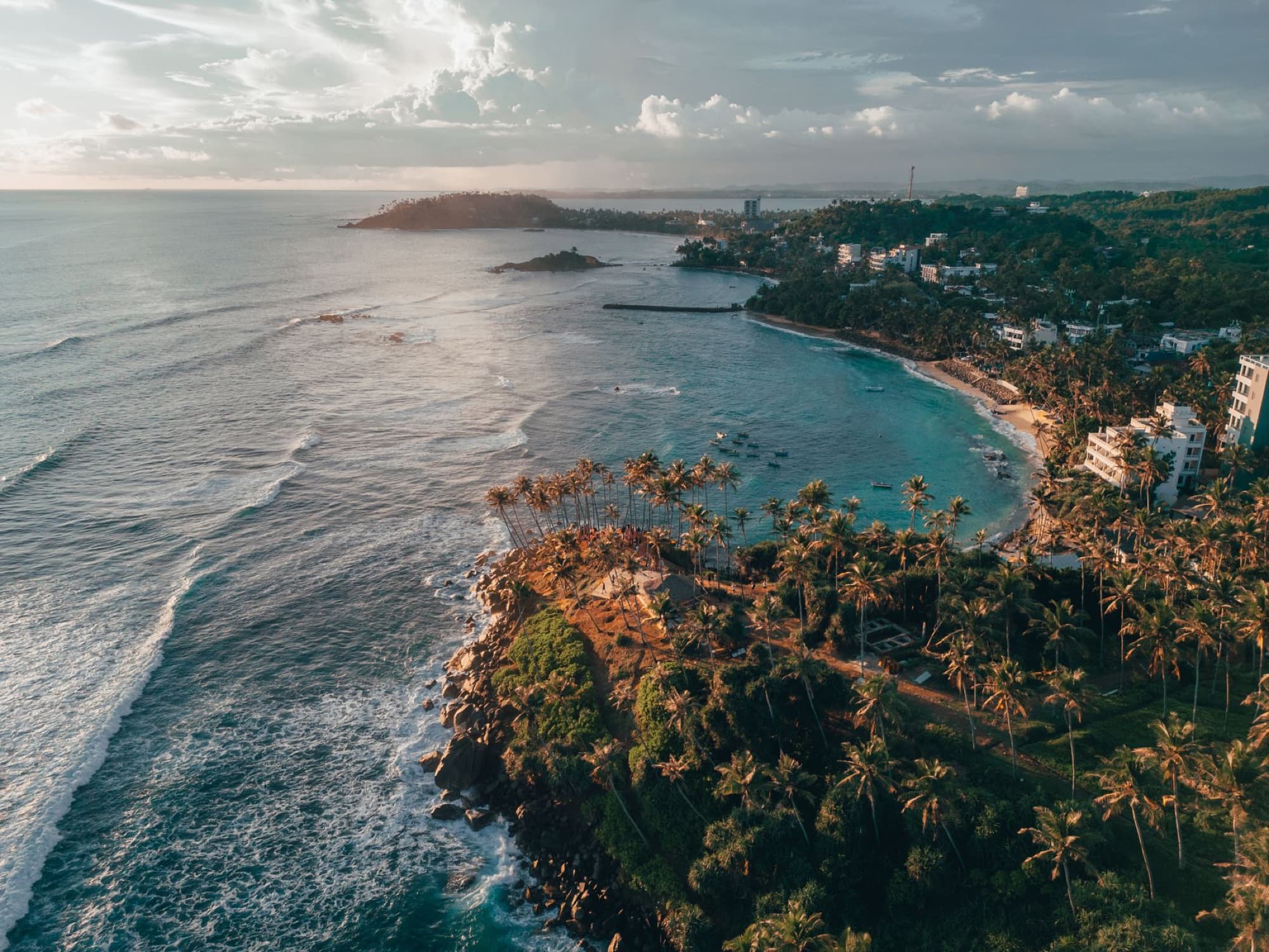 Stunning aerial view of Sri Lankan coastline with waves, cliffs, and lush palm trees at sunset.