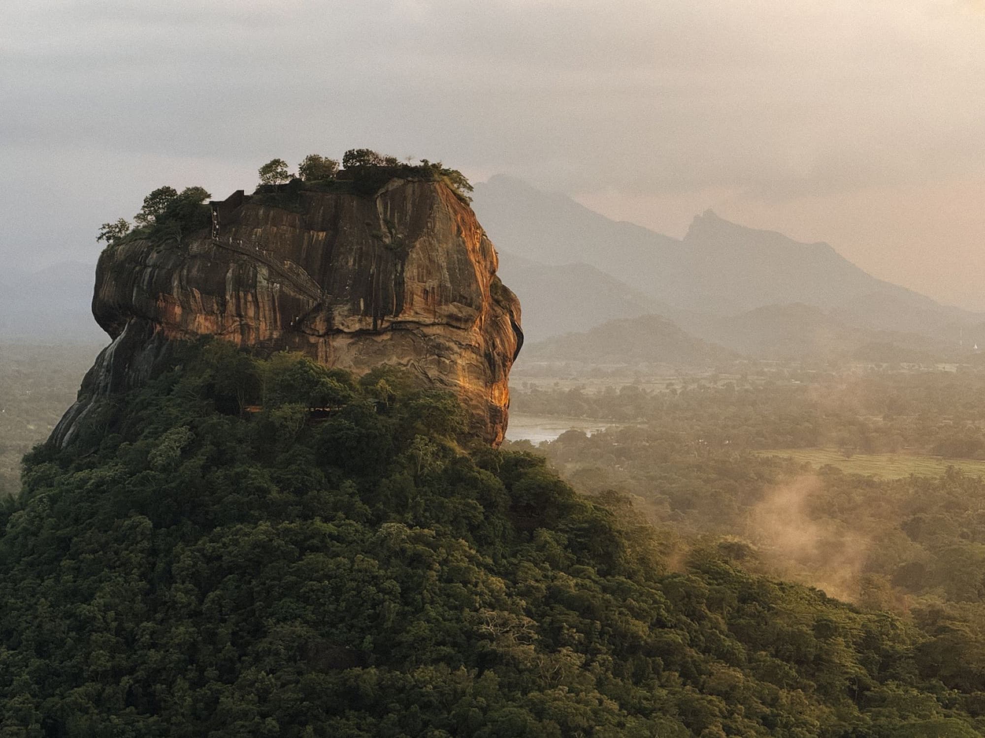Stunning aerial view of Sigiriya Rock, lush landscape, and distant mountains in Sri Lanka.