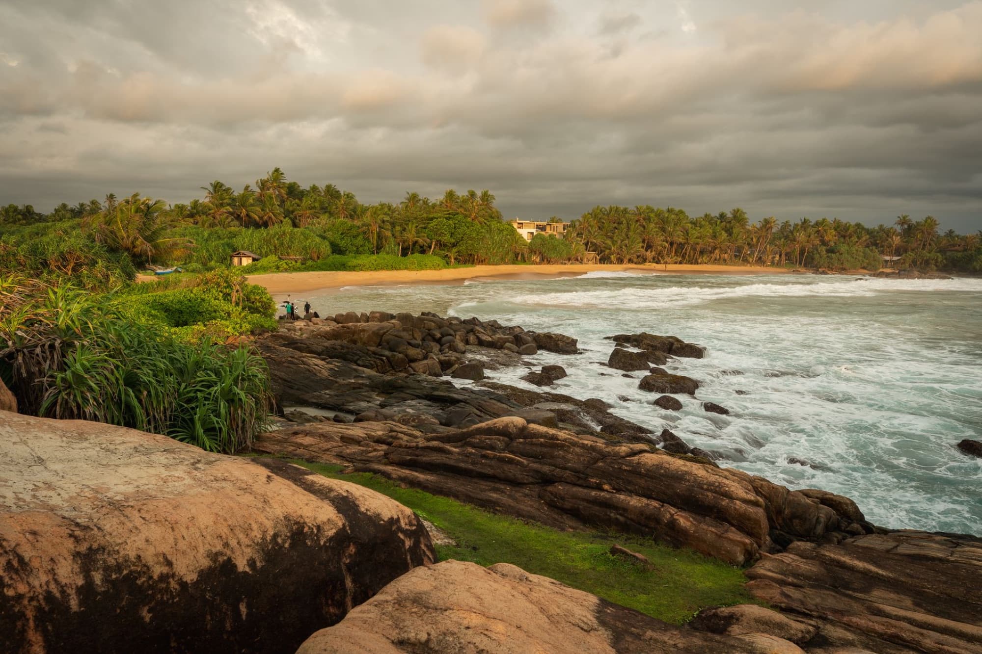 Serene tropical beach with lush greenery and rocky coastline at sunset in Sri Lanka.