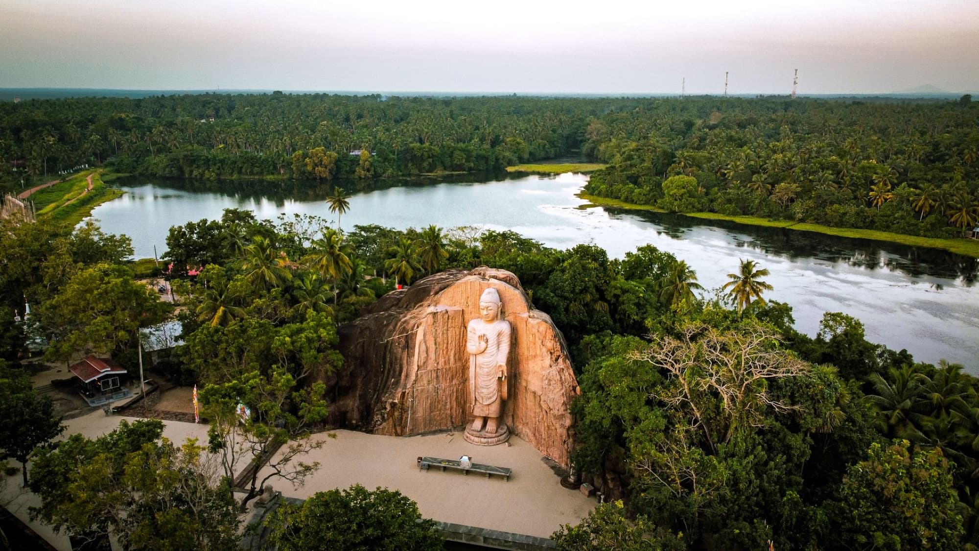Aerial photograph showcasing the serene Avukana Buddha statue surrounded by lush greenery and a calm river in Sri Lanka.