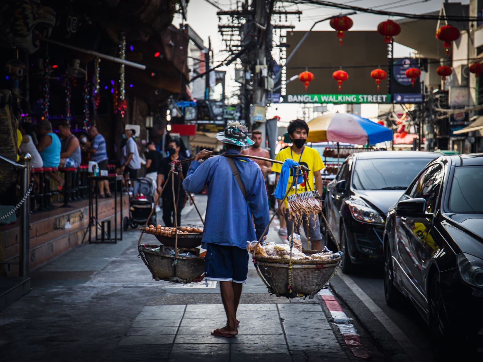 A street vendor carrying baskets full of goods on the lively Bangla Walking Street in Thailand.