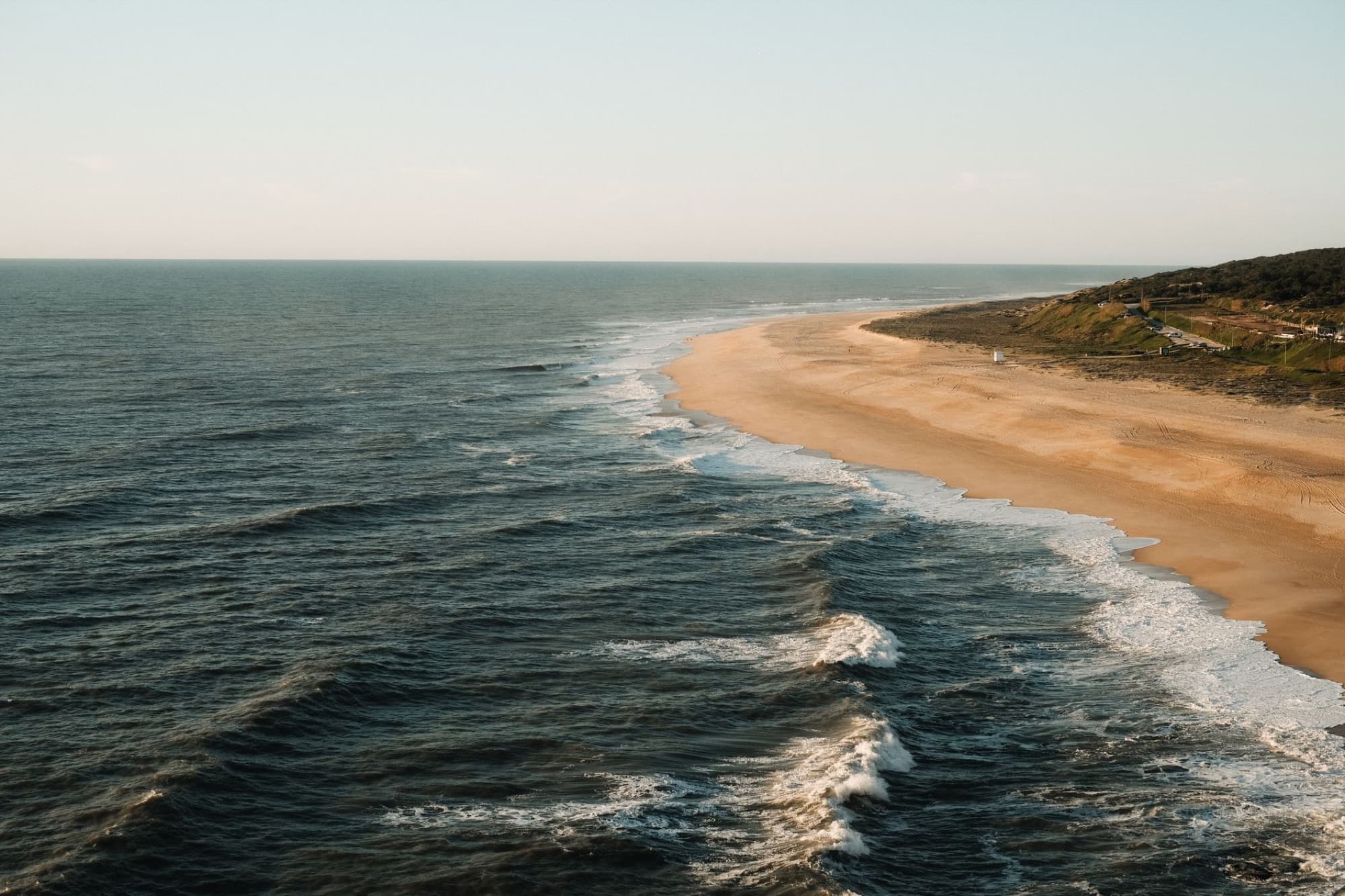Aerial view of a tranquil beach and ocean waves on a sunny day, with golden sand and blue waters.