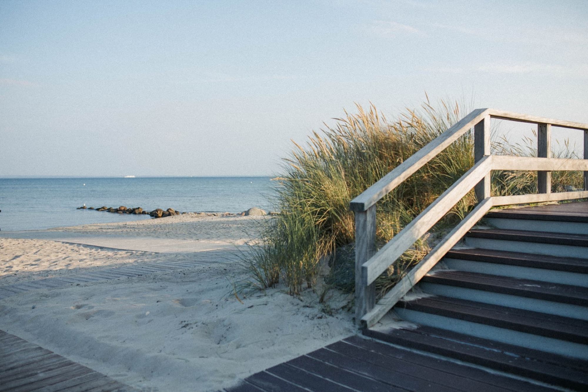 Scenic view of a wooden pathway leading to a tranquil sandy beach with gentle ocean waves.