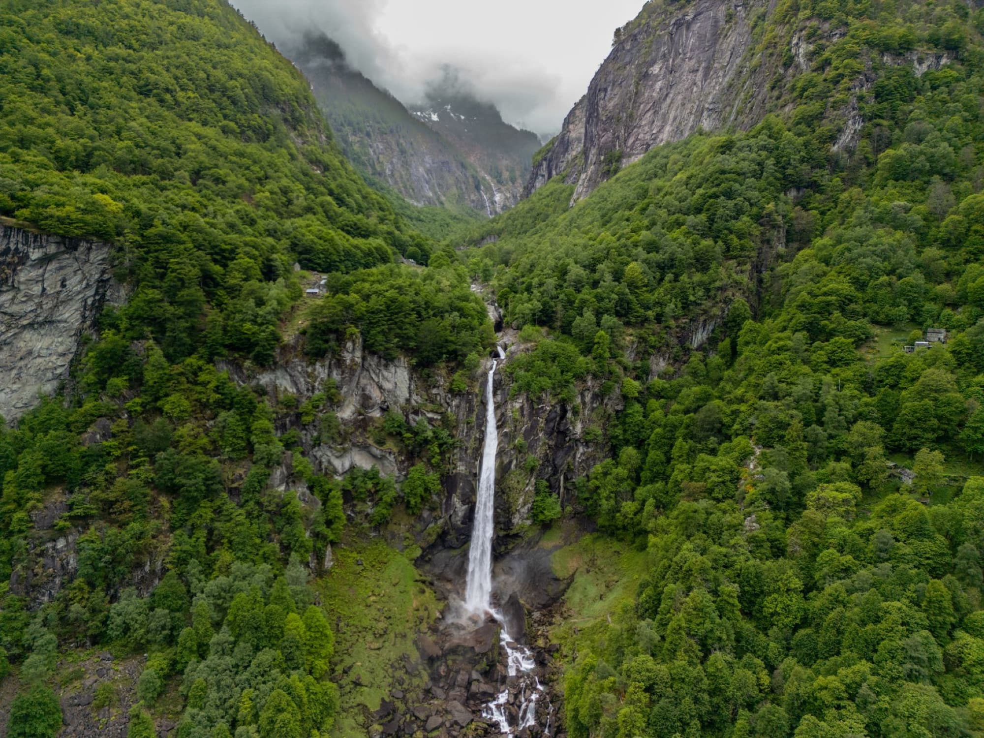 Stunning aerial shot of a lush green valley with a cascading waterfall in Cevio, Ticino, Switzerland.