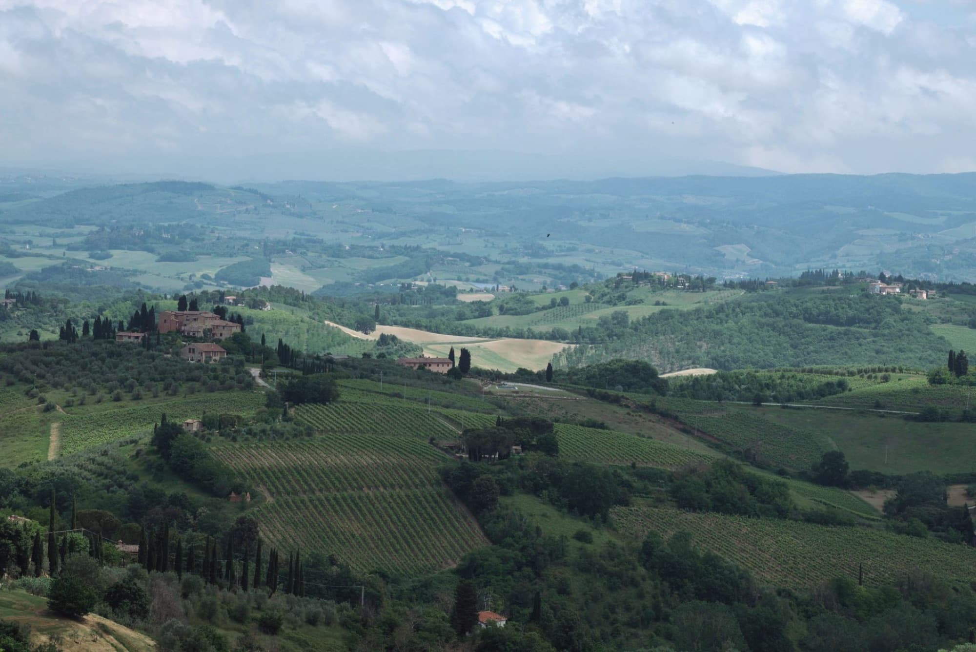 Stunning aerial shot of Tuscany's rural landscape with vineyards and rolling hills under a cloudy sky.
