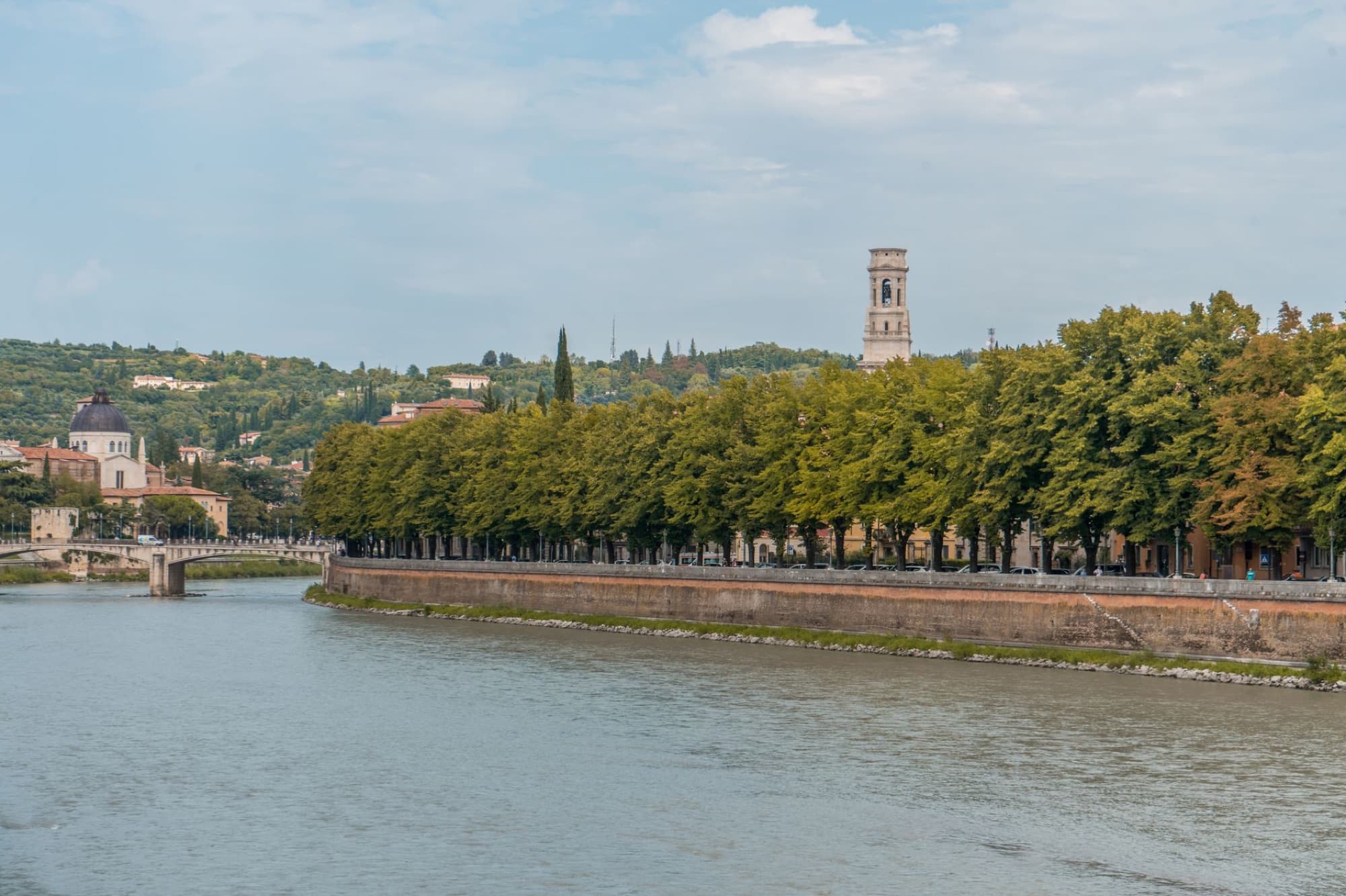 Picturesque scene of Verona's riverside with lush trees and historic architecture, capturing the essence of Veneto, Italy.