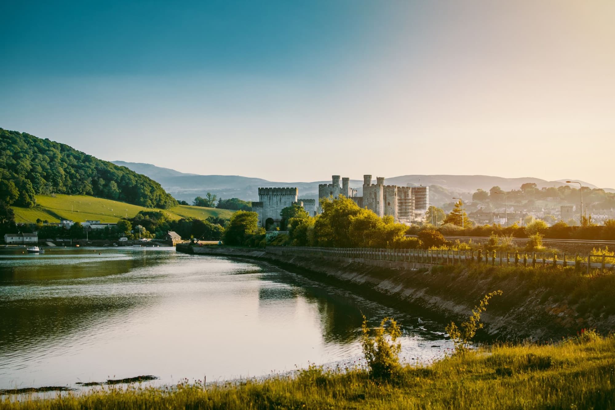 Beautiful sunrise view of Conwy Castle in Wales, with reflective water and lush landscape.