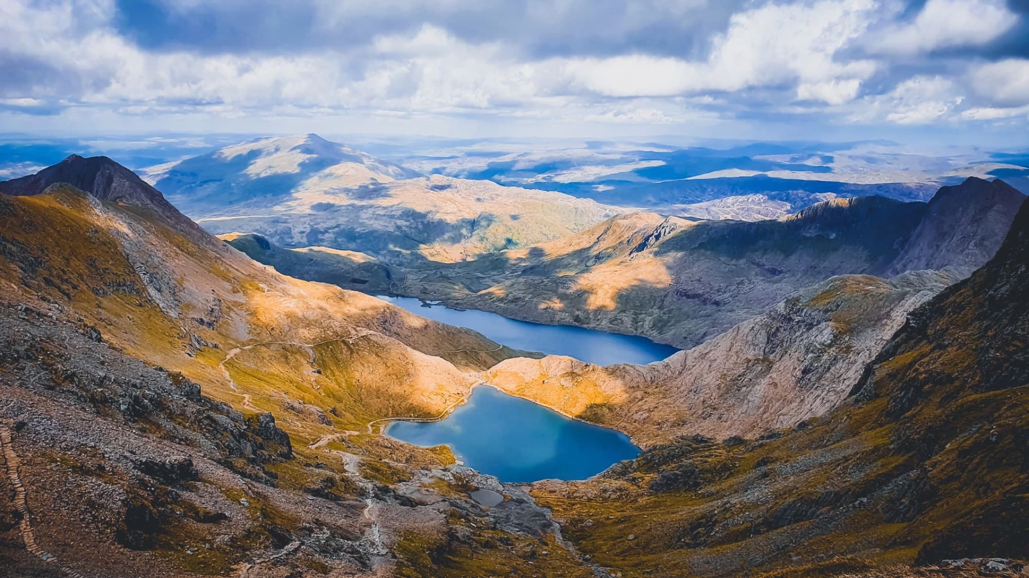 Breathtaking view of the Snowdonia mountain range with a scenic lake and rolling hills, captured in Wales.