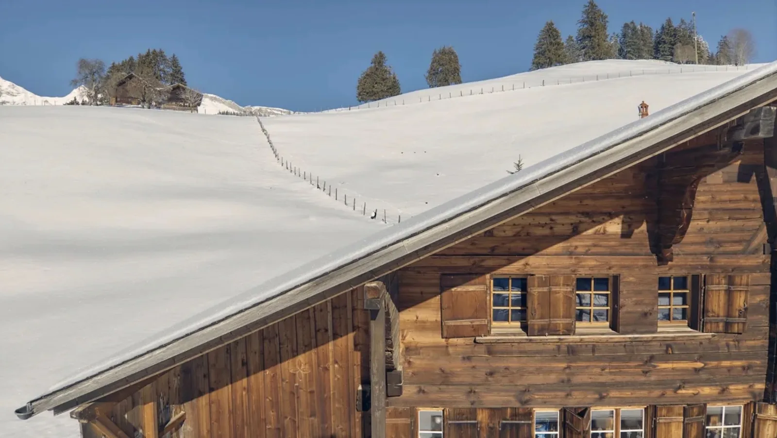 The deep eaves and weathered timber façade of a Saanenland chalet beside a snow-covered slope